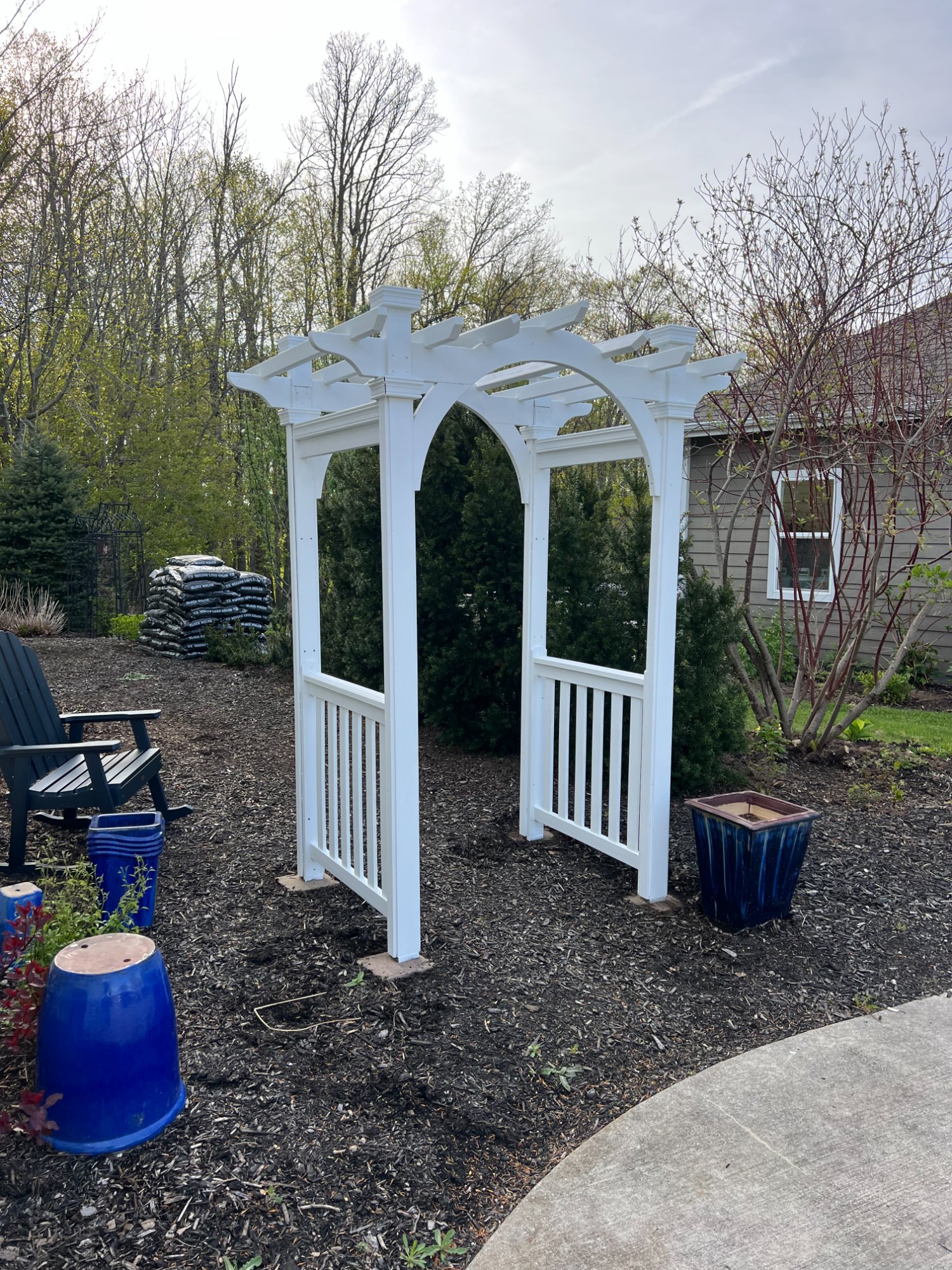 Freshly painted white garden arbor from alternate angle showing arched top and landscaping